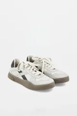 Zapatillas urbanas de cuero en tono off-white, con detalles en color marrón oscuro y suela de goma texturizada en contraste. Presentan cordones al tono y logo de la marca grabado en el lateral.