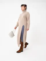 Buzo largo gris de tejido de punto grueso con cuello alto y capucha con orejas de conejo rojas. Tiene mangas largas y un tajo lateral.