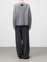 Cardigan gris melange de lana con cuello en pico y cierre frontal de botones. Presenta un diseño de punto calado en el cuerpo y mangas largas con acabado en canalé.
