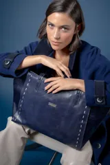 Bolso tipo shopper de cuero azul marino, con laterales texturizados y detalle de costuras visibles en los bordes. Incluye placa metálica con el logo de la marca en el frente.