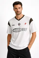 Remera de algodón con cuello en V, manga corta y diseño holgado. Presenta un estampado frontal con la palabra 'SUCCESS' y detalles gráficos en el pecho, con bloques de color negro en los hombros.
