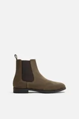 Bota estilo Chelsea de piel con acabado serraje color verde militar. Presenta elásticos laterales en tono marrón oscuro para facilitar el calce, horma redonda y suela a tono con ligero tacón.