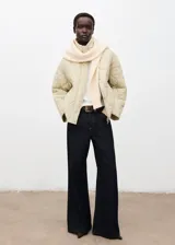 Campera acolchada de diseño oversize en color beige, con cuello alto, cierre frontal de cremallera y botones, y bolsillos laterales.