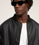 Campera estilo bomber de poliuretano (PU) símil cuero en color negro, con cuello, puños y dobladillo acanalados, y cierre frontal de cremallera.