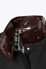 Chaqueta negra de la colección Zara Woman, confeccionada en hilatura con mezcla de algodón. Presenta un cuello alto brillante en contraste de color marrón oscuro, manga larga, bolsillos delanteros y pespuntes marcados. El forro interior es a contraste y el cierre frontal es con botones.