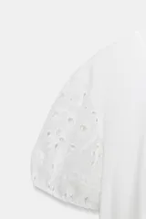 Camiseta blanca de manga corta abullonada y cuello redondo, con detalles de bordados perforados y bajo con doble volante.