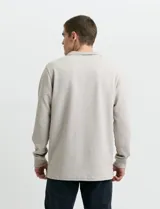 Remera de manga larga con cuello polo, confeccionada en tejido de punto canalé francés. Presenta abotonadura frontal con botones de madera y detalles a contratono en la cartera y el interior del cuello.