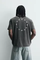 Camiseta de corte relajado con cuello redondo y mangas cortas. Presenta un efecto lavado que le otorga una apariencia única y estampados a contraste en el frente.