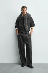 Pantalón de jeans de algodón ligero, color negro lavado, con corte balloon fit (holgado y ancho). Presenta pliegues frontales marcados en la cintura y cierre frontal de cremallera y botón.