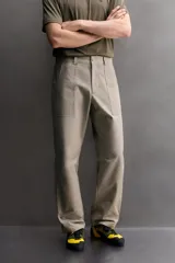 Pantalón de corte tapered fit color beige, confeccionado en tejido ligero de algodón con estructura rip stop. Cuenta con bolsillos de plastrón delanteros con acceso curvado, pinzas en las rodillas para mayor movilidad, y cierre frontal con cremallera y botón a presión.