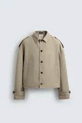 Cazadora color beige, estilo cropped, con cuello de solapa, manga larga con puños ajustables y trabillas en los hombros. Presenta bolsillos de vivo en la cadera y cierre frontal de botonadura.