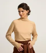 Blusa de punto color beige con cuello alto y mangas largas con puños acanalados. Diseño básico y ajustado al cuerpo, confeccionada en tejido de viscosa, poliéster y poliamida.
