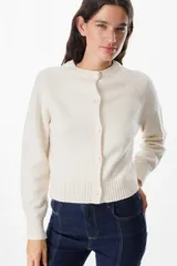 Saco tipo cardigan de punto color crudo, con cuello redondo, cierre frontal de botones y mangas largas con puños acanalados.