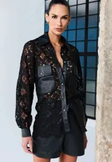 Camisa negra de encaje con detalles en cuero sintético, que incluyen el cuello, la tapeta de botones a presión, los bolsillos frontales con solapa, los puños y el borde inferior. Presenta mangas largas y un diseño estructurado y sofisticado.