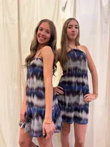 Vestido corto con escote halter y cuello alto, con tiras ajustables en el cuello. Presenta un diseño estampado con efecto tie-dye en tonos azul, negro y blanco, con espalda abierta y elástico en la cintura.