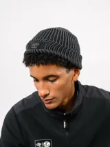 Gorro tipo beanie de tejido acanalado en color azul, con parche rectangular rojo en el frente que presenta el logo de la marca Umbro bordado en blanco.
