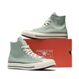 Championes Converse modelo Chuck 70 Hi, de caña alta, confeccionados en lona de algodón color verde salvia. Presentan el icónico parche de estrella en el tobillo, puntera de goma reforzada y entresuela de goma color crema con detalles en negro.