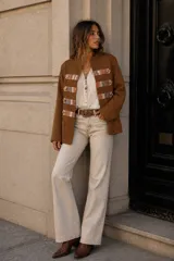 Chaqueta de estilo militar en color marrón, confeccionada en tejido de lana. Presenta un diseño estructurado con cuello mao y detalles decorativos en los laterales frontales con aplicaciones de tela a cuadros y botones metálicos.