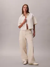 Camisa de denim de corte cropped y mangas cortas, con cuello clásico y cierre frontal de botones. Presenta un diseño minimalista y estructurado.