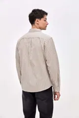 Camisa de corte regular confeccionada en algodón, con diseño de rayas verticales finas en color beige y negro. Presenta cuello clásico, cierre frontal con botones y un bolsillo en el pecho con el logo de la marca bordado.