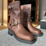 Bota de cuero vacuno color negro, con hebillas ajustables, cierre interno y suela de goma artesanal.