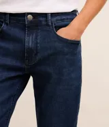 Pantalón de jean azul oscuro para hombre, con corte slim, diseño clásico de cinco bolsillos, trabillas para cinturón y cierre frontal con botón y cremallera.