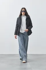 Campera puffer negra con diseño acolchado, capucha integrada y cierre frontal con botones a presión. Presenta puños elásticos y costuras decorativas en el frente.