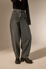 Pantalon de jean estilo barrel con lavado oscuro, tiro medio y detalle de tachas metálicas a lo largo de las costuras laterales.