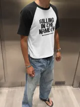 Remera oversize de corte raglan, color blanco con mangas y cuello en contraste negro. Presenta estampado frontal con la inscripción "KILLING IN THE NAME OF" y el texto secundario "NOW YOU DO WHAT THEY TOLD YA".