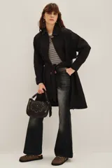 Trench negro de corte midi con cuello camisero, cierre frontal y cinturón ajustable a la cintura. Presenta mangas largas con puños rectos y un diseño minimalista y versátil.