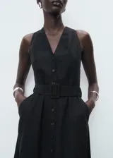 Vestido midi negro sin mangas, con cuello en V, cierre frontal con botones y cinturón ajustable del mismo tejido. Diseño evasé con mezcla de lyocell y lino.