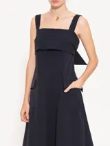 Vestido midi negro de poplin con lycra, silueta línea A, bolsillos plaqué en los laterales y tajo en el centro delantero. Se ajusta en la espalda mediante un lazo.