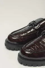 Mocasín de cuero vacuno color marrón con acabado charol, forro y plantilla de cuero vacuno y suela de goma.