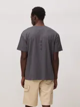 Remera de corte oversize color gris oscuro, con cuello redondo y pequeño detalle bordado en forma de cruz en el centro del pecho.