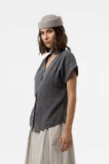 Camisa gris de corte relajado, con escote en V y lazo largo incorporado en el cuello. Mangas cortas con vuelta y frunce sutil en los hombros.