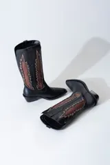 Bota texana de cuero negro con apliques de cuero marrón en los laterales y pespuntes en color crema. De caña media/alta y taco bajo. Diseño calado con motivos geométricos.