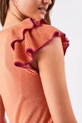 Top color salmón metalizado, de algodón peinado, con cuello redondo y mangas cortas con volados con borde fucsia.