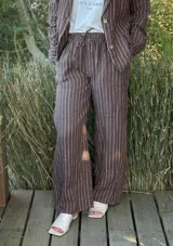 Pantalón de corte ancho y relajado, confeccionado en lino con diseño de rayas verticales. Presenta cintura elástica con cordón de ajuste y bolsillos laterales.