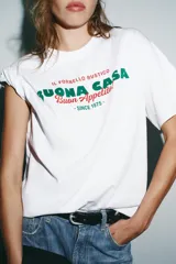 Camiseta blanca de manga corta y cuello redondo con estampado frontal en verde y rojo que dice "IL FORNELLO RUSTICO BUONA CASA Buon Appetito! - SINCE 1975 -".
