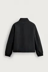 Cazadora técnica de corte holgado color negro, con cuello solapa, cierre frontal de cremallera metálica, bolsillos frontales ribeteados y puños con elástico.