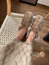 Sandalias de cuero negro con diseño de tiras entrelazadas, estilo huarache, con pulsera ajustable al tobillo mediante hebilla metálica.