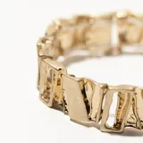 Brazalete rígido dorado con eslabones rectangulares texturizados.