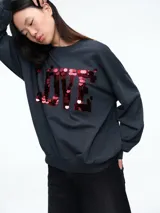 Buzo de algodón color gris oscuro, con cuello redondo, mangas largas y puños elásticos. Presenta la palabra LOVE estampada en el frente con aplicaciones de lentejuelas rojas.