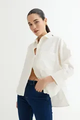 Camisa de manga larga color blanco roto, de corte holgado y estilo rústico, con cuello camisero y un bolsillo de parche en el pecho.