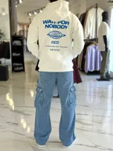 Canguro oversize blanco con capucha y bolsillo tipo canguro, confeccionado con tela de felpa suave. Presenta estampado azul en la espalda con la inscripción "WAIT FOR NOBODY", un diseño de planeta con el año 2021, el logo "STWD" y las frases "CHASE YOUR DREAMS, DON'T SLOW DOWN" y "TOP STYLE".