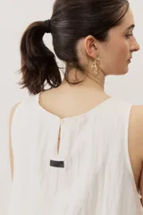Vestido corto blanco sin mangas, con cuello redondo y detalle de nudo drapeado en el lateral.