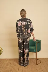 Conjunto de dos piezas compuesto por una campera bomber y un pantalón ancho, ambos confeccionados en satén negro con estampado floral y de aves. La campera cuenta con cierre frontal y puños elastizados, mientras que el pantalón tiene tiro alto y cintura elástica con cordón ajustable.