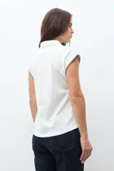 Remera de cuello polo en color crudo, con mangas cortas y detalle de bordado en contraste a lo largo del escote y en los bordes de las mangas.