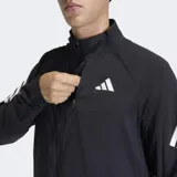 Campera deportiva Adidas de corte clásico, color negro con detalles en blanco. Presenta cierre frontal, cuello alto, bolsillos con cremallera y las icónicas tres bandas de la marca en las mangas. Incluye inserciones de malla para mayor ventilación y dobladillo con cordón elástico ajustable.