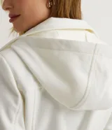 Campera alargada de polivelour color blanco, con cuello alto que se pliega y se ata a la cintura, mangas largas, abotonado frontal doble, bolsillos y cinturón.